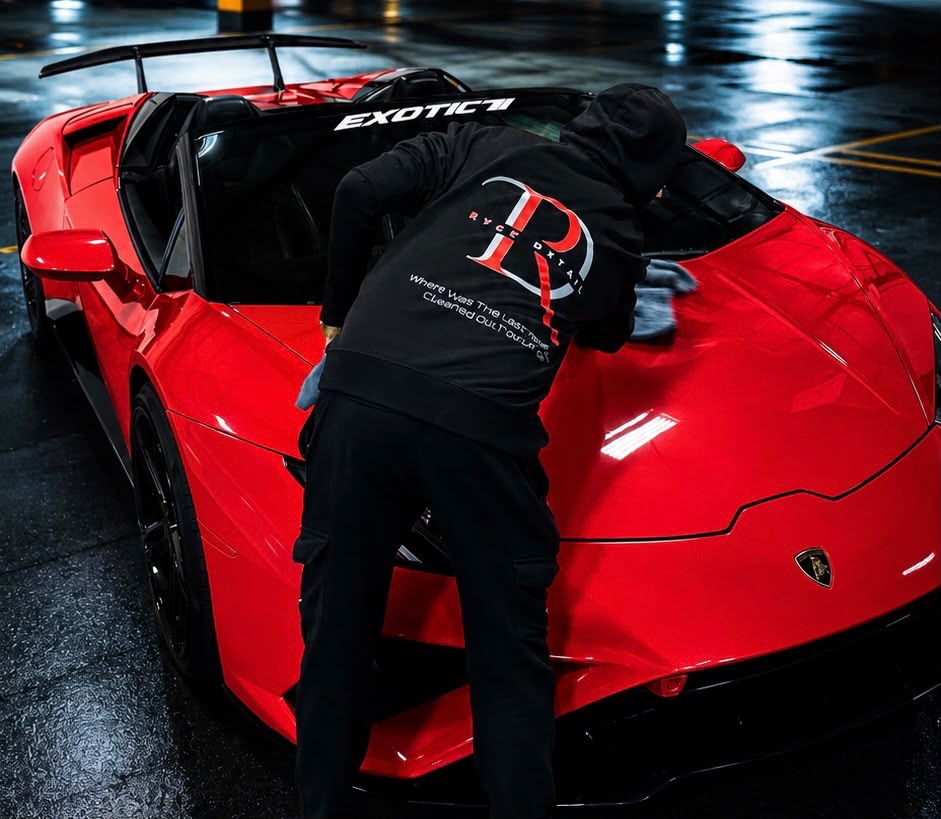Detailer hand-wiping the hood of a red sports car